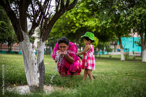 portrait of cute indian mother and daughter watering in the park.