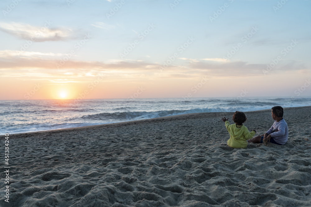 Fototapeta premium Two young caucasian kids at sunset on the northern beach in portugal pointing at the setting sun.