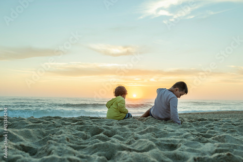 Two young caucasian kids at sunset on the northern beach in portugal pointing at the setting sun. © Juan