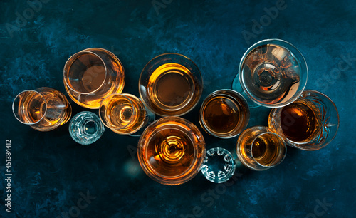 Strong alcohol drinks, hard liquors, spirits and distillates iset in glasses: cognac, scotch, whiskey and other. Blue background, top view