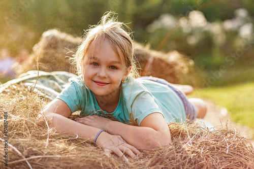 Portrait of a smiling 9-year-old blonde girl lying on a haystack. Happy childhood. A hot summer evening.