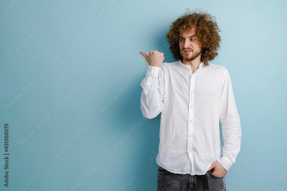 Young curly man with ginger hair grimacing and pointing finger aside Young curly man with ginger hair grimacing and pointing finger aside
