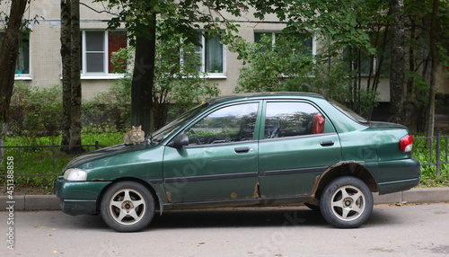 An old dark green car with a cat on the hood in the courtyard of a residential building  Bolshnevikov Avenue  St. Petersburg  Russia  August 2021