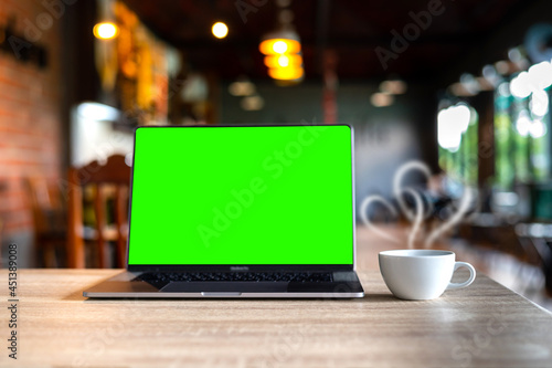 Laptop with Green screen on table. white coffee cup with smoke on blurred coffee shop background.