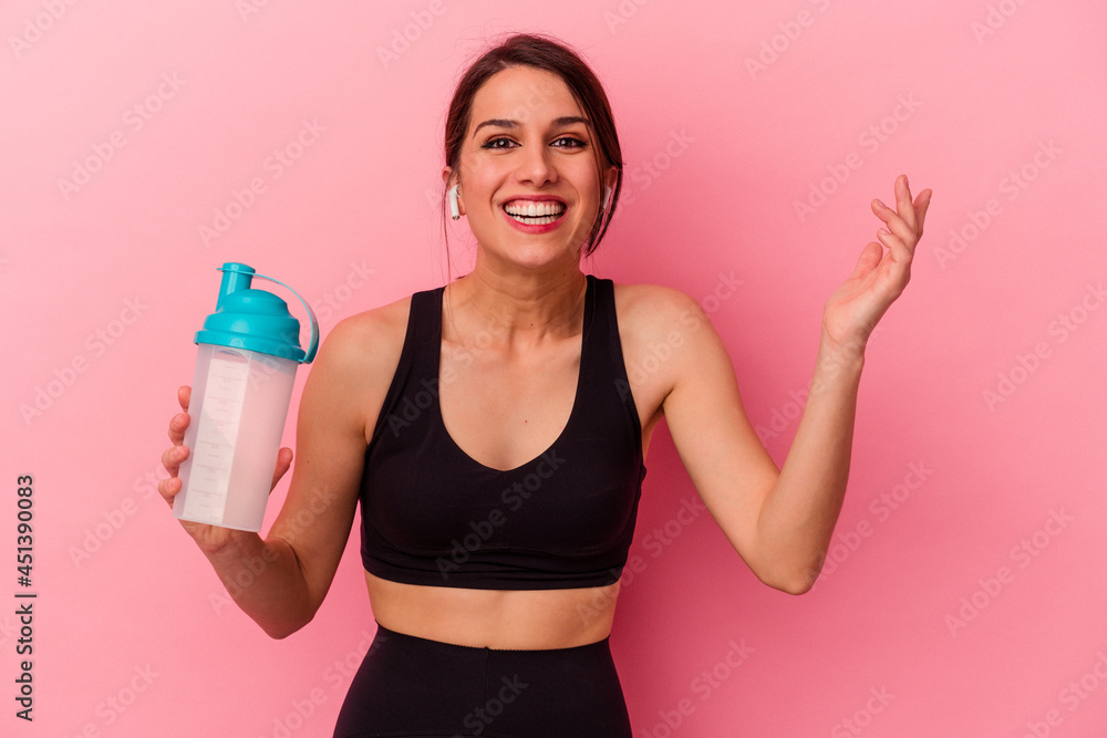 Young caucasian woman drinking a protein shake isolated on pink background receiving a pleasant surprise, excited and raising hands. Young caucasian woman drinking a protein shake isolated on pink background receiving a pleasant surprise, excited and raising hands.