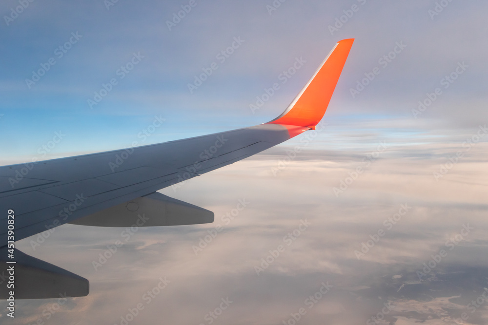 view of the blue clear sky from the height of flight above the clouds from the window of the plane in the bright sun. part of an airplane wing in the frame
