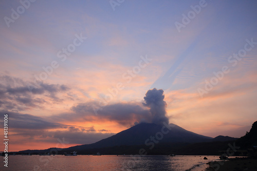 爆発する桜島の噴煙がオレンジ色に染まっている空に飛行機雲