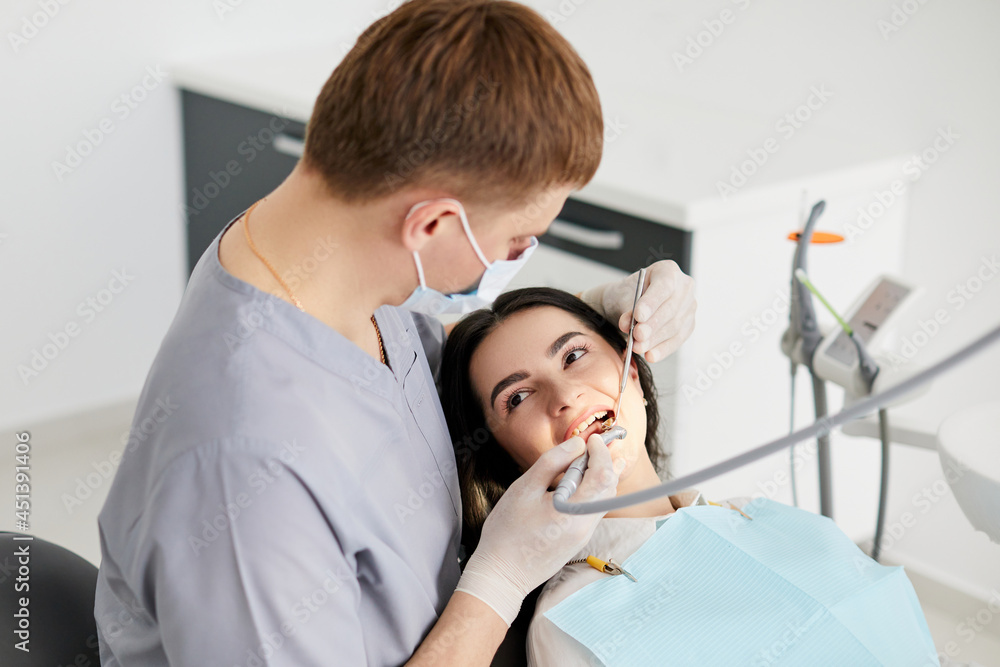 Fototapeta premium Beautiful young woman doing tooth examination in the dental office. Portrait of smiling girl on a dental chair in dentistry