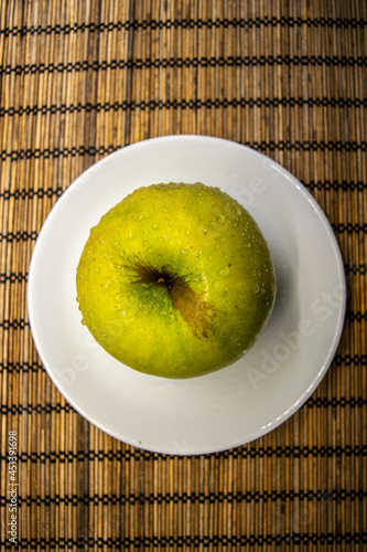 big ripe yellow green apple with brown line and water drops on a white small plate bamboo mat
