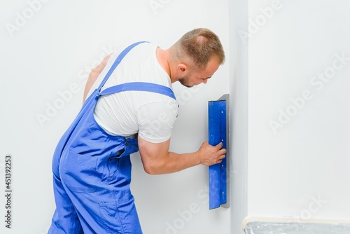 The builder carefully corrects the irregularities of the wall with a trowel. Builder in work clothes against a gray wall. Photo plasterer at work.