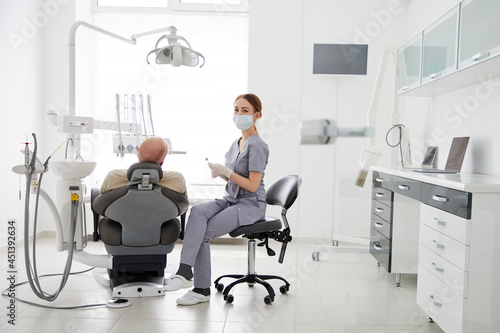 Portrait of young female dentist standing by mid adult man in clinic. Female dentist repairing patient tooth in dental ambulant