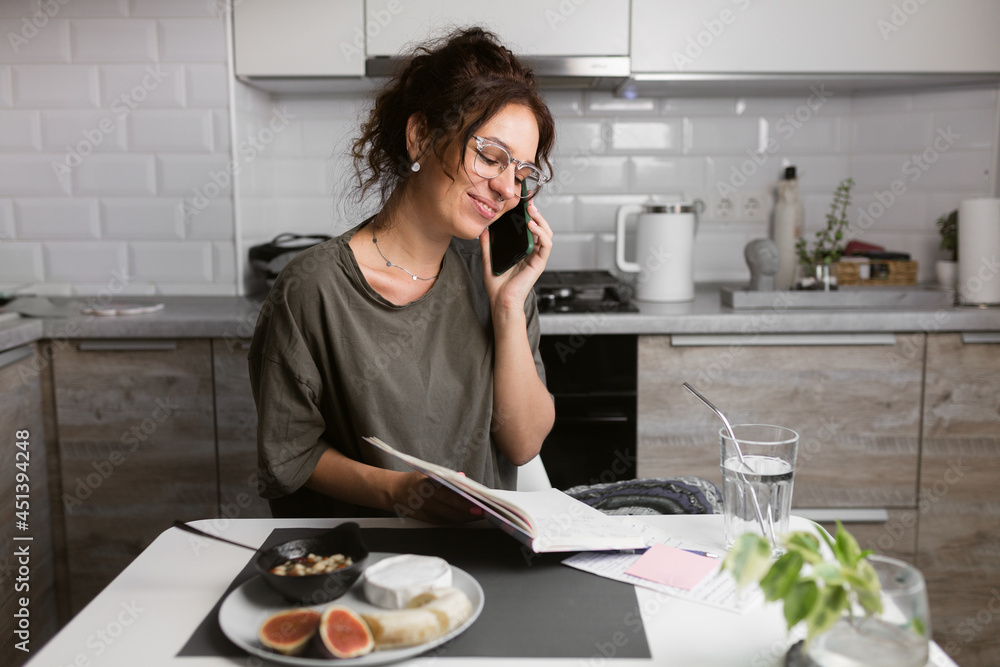 business woman wearing casual home t shirt doing paper works on the kitchen while having breakfast, making notes to daybook