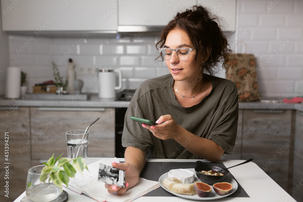 beautiful girl in glasses with curly hair eating breakfast on the kitchen and talking on the phone