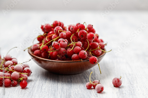 Frozen red currants in a brown ceramic vase on a white wooden table. Close-up.