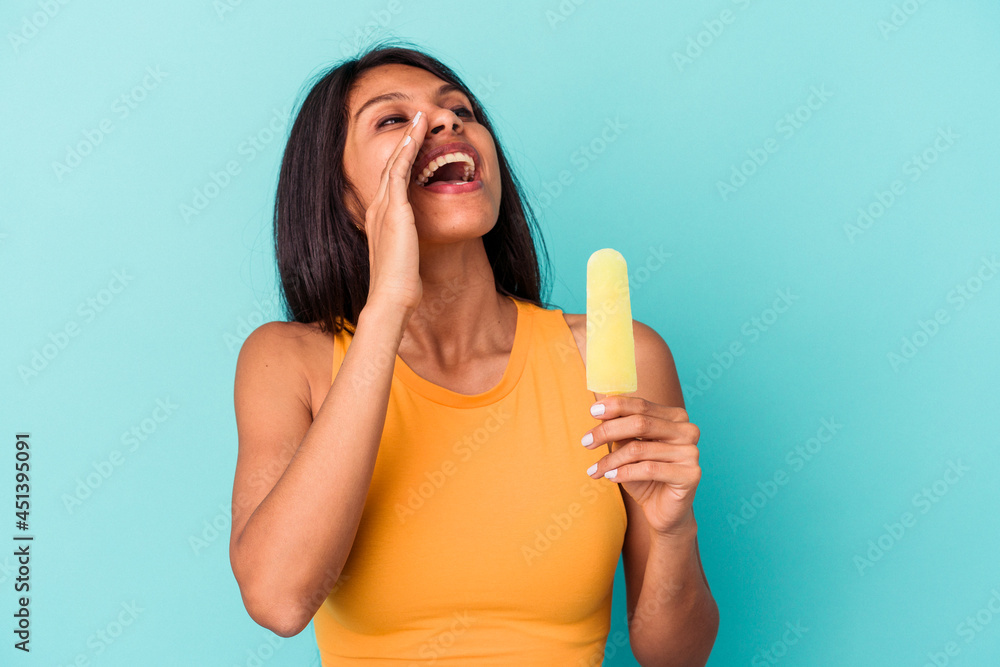 Young latin woman holding ice cream isolated on blue background shouting and holding palm near opened mouth. Young latin woman holding ice cream isolated on blue background shouting and holding palm near opened mouth.