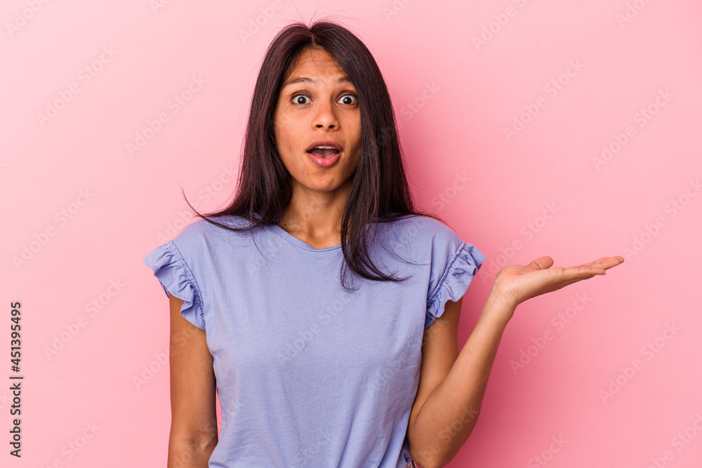 Young latin woman isolated on pink background impressed holding copy space on palm. Young latin woman isolated on pink background impressed holding copy space on palm.