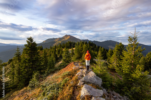 Landscape with beautiful cloudy sky. Autumn morning mountains. Successful sporty girl is standing at the lawn in orange jacket. Wallpaper background. A place to relax Carpathian, Ukraine, Europe. photo