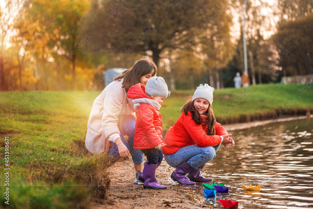 Fototapeta premium Children play with boats on the river bank. sunny autumn. yellow park. blue river at sunset