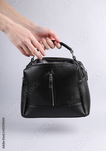 Female hand holding black leather bag on gray background
