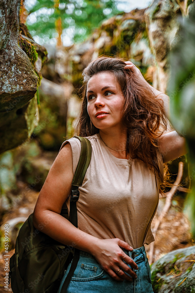 A young woman tourist is hiking in a dense forest with huge stones with moss. A young woman tourist is hiking in a dense forest with huge stones with moss.