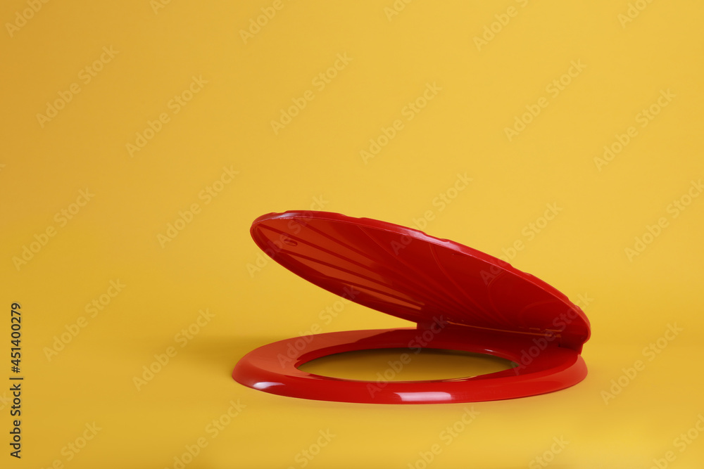 New red plastic toilet seat on yellow background New red plastic toilet seat on yellow background
