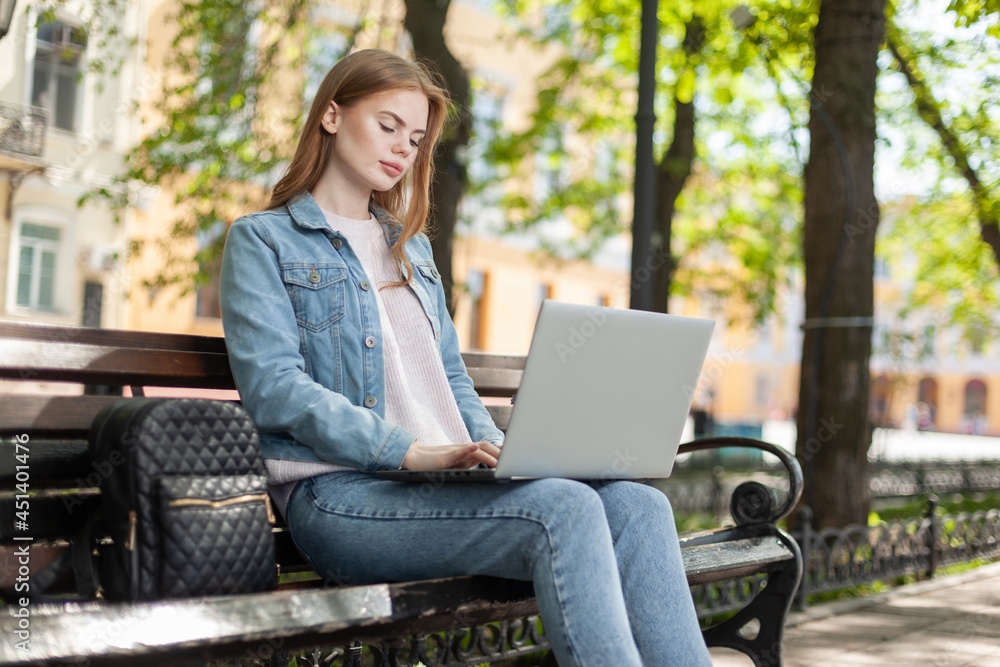 Young pretty woman student or freelancer using laptop while sitting on a bench in the city Young pretty woman student or freelancer using laptop while sitting on a bench in the city