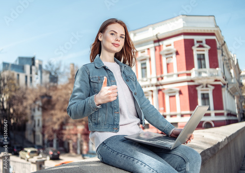 Cute caucasian woman with laptop showing thumbs up in the city