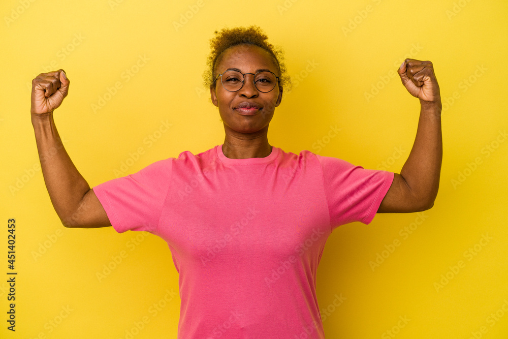 Fototapeta premium Young african american woman isolated on yellow background showing strength gesture with arms, symbol of feminine power