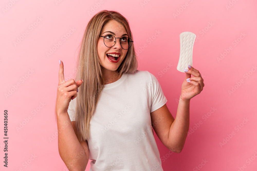 Young russian woman holding a compress isolated on pink background pointing upside with opened mouth. Young russian woman holding a compress isolated on pink background pointing upside with opened mouth.