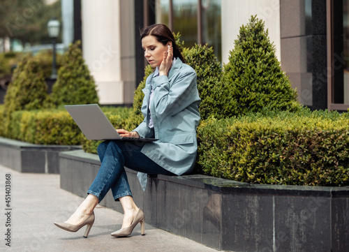 Cute Caucasian woman is using laptop in the city outdoors. Distant work. Modern business woman. Lifestyle
