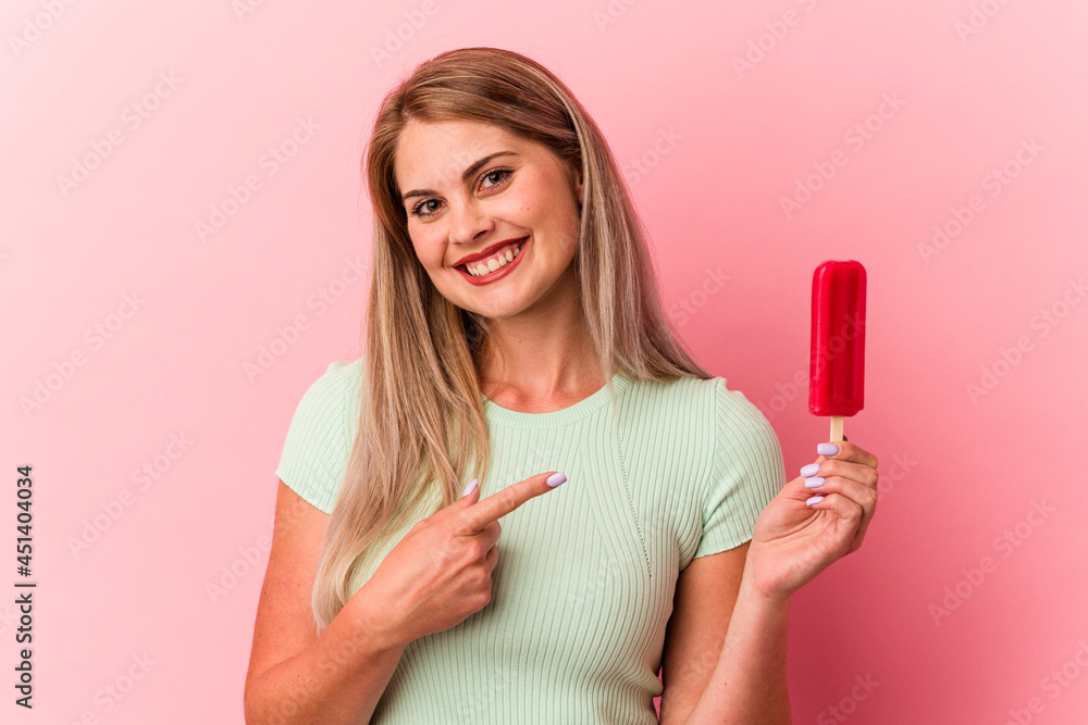 Young russian woman holding an ice cream isolated on pink background smiling and pointing aside, showing something at blank space. Young russian woman holding an ice cream isolated on pink background smiling and pointing aside, showing something at blank space.