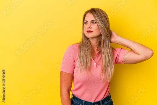 Young russian woman isolated on yellow background touching back of head, thinking and making a choice.