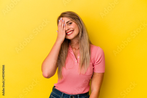 Young russian woman isolated on yellow background having fun covering half of face with palm.