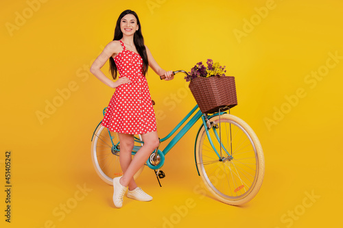 Portrait of lady with bike hand hip wear dotted red mini dress footwear on yellow background © Tetiana