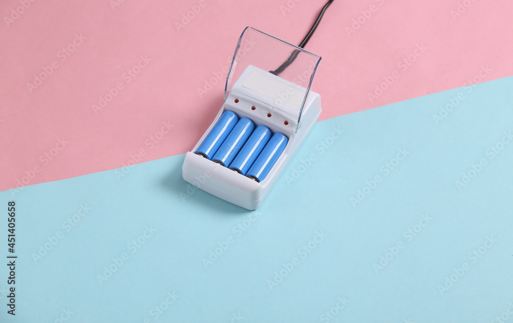 Fototapeta premium Battery charger with AA rechargeable batteries on blue pink pastel background