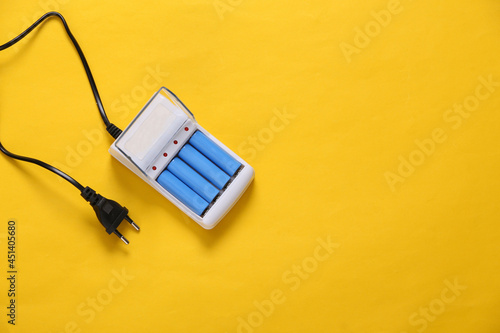 Foto Battery charger with AA rechargeable batteries on yellow background
