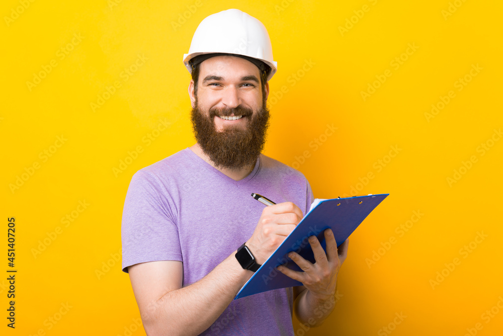 Smiling engineer bearded man is writing in some papers over yellow background. Smiling engineer bearded man is writing in some papers over yellow background.