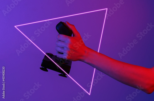 Hands holding retro joystick in blue-red neon gradient light with triangle. Old gaming. 80s retro wave photo