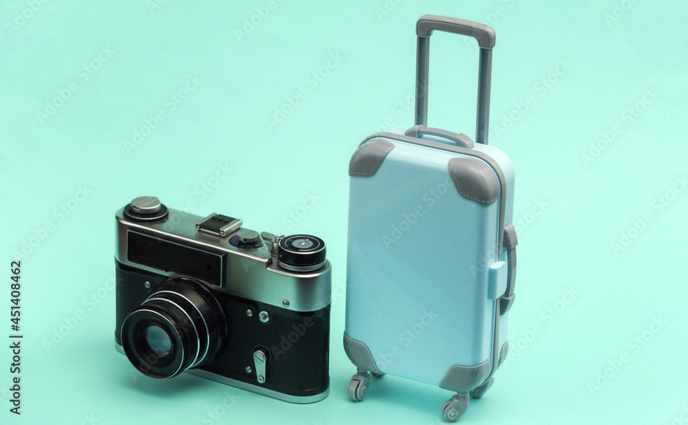 Travel or trip concept. Mini plastic travel suitcase and camera on blue pastel background. Minimal style Travel or trip concept. Mini plastic travel suitcase and camera on blue pastel background. Minimal style