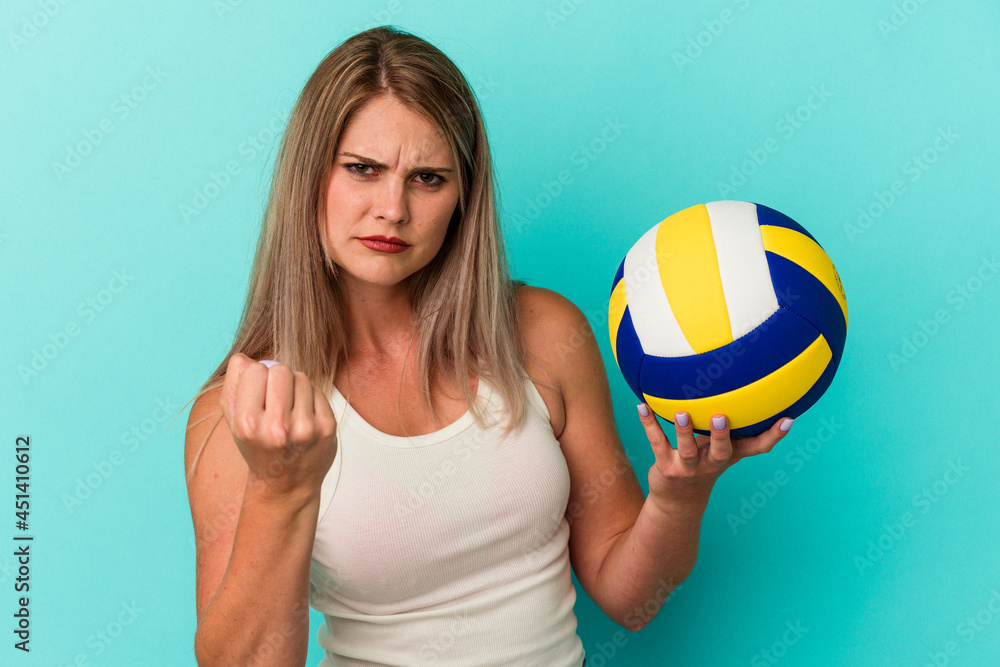 Young russian woman playing volleyball isolated on blue background showing fist to camera, aggressive facial expression.