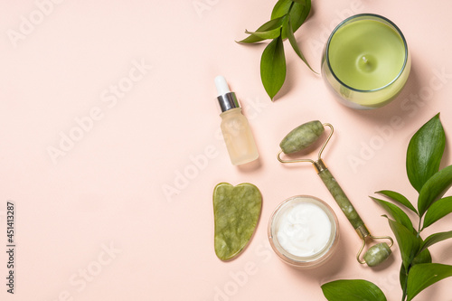 Cosmetic products - Jade roller and gua sha massager with cream and serum bottles at pastel background. Spa background. Top view with copy space.