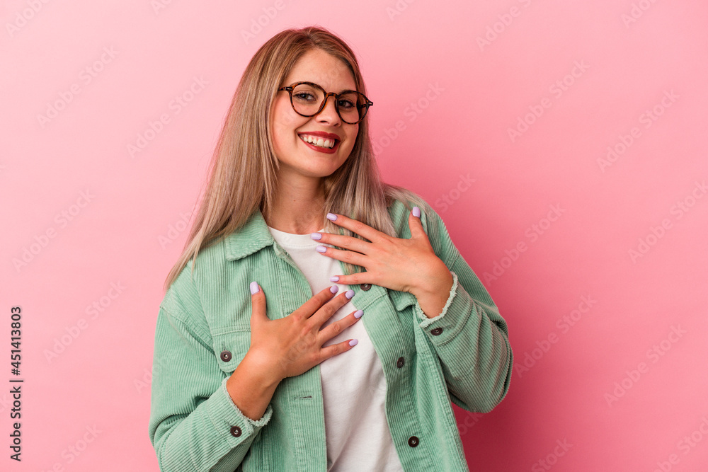 Young russian woman isolated on pink background laughs happily and has fun keeping hands on stomach.