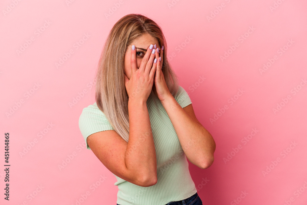 Young russian woman isolated on pink background blink at the camera through fingers, embarrassed covering face. Young russian woman isolated on pink background blink at the camera through fingers, embarrassed covering face.