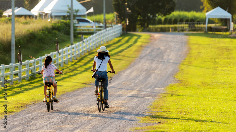 Family Happy. Mother and daughter smiling happy outdoor with bicycling at the garden meadow in sunset. Lifestyle Family Concept Family Happy. Mother and daughter smiling happy outdoor with bicycling at the garden meadow in sunset. Lifestyle Family Concept