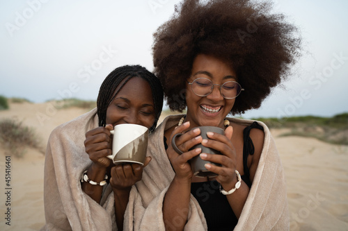 Cheerful black girlfriends drinking coffee on beach photo