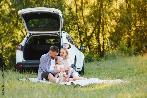 Young family three people in white clothes have picnic. Beautiful parents and daughter travel by car during summer vacation. © Serhii