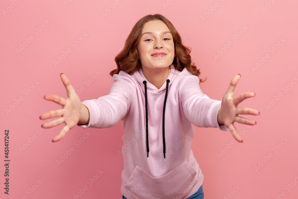 Portrait of happy friendly teen girl in hoodie giving free hugs with outstretched hands, inviting to embrace, welcoming and supporting. Indoor studio shot isolated on pink background Portrait of happy friendly teen girl in hoodie giving free hugs with outstretched hands, inviting to embrace, welcoming and supporting. Indoor studio shot isolated on pink background