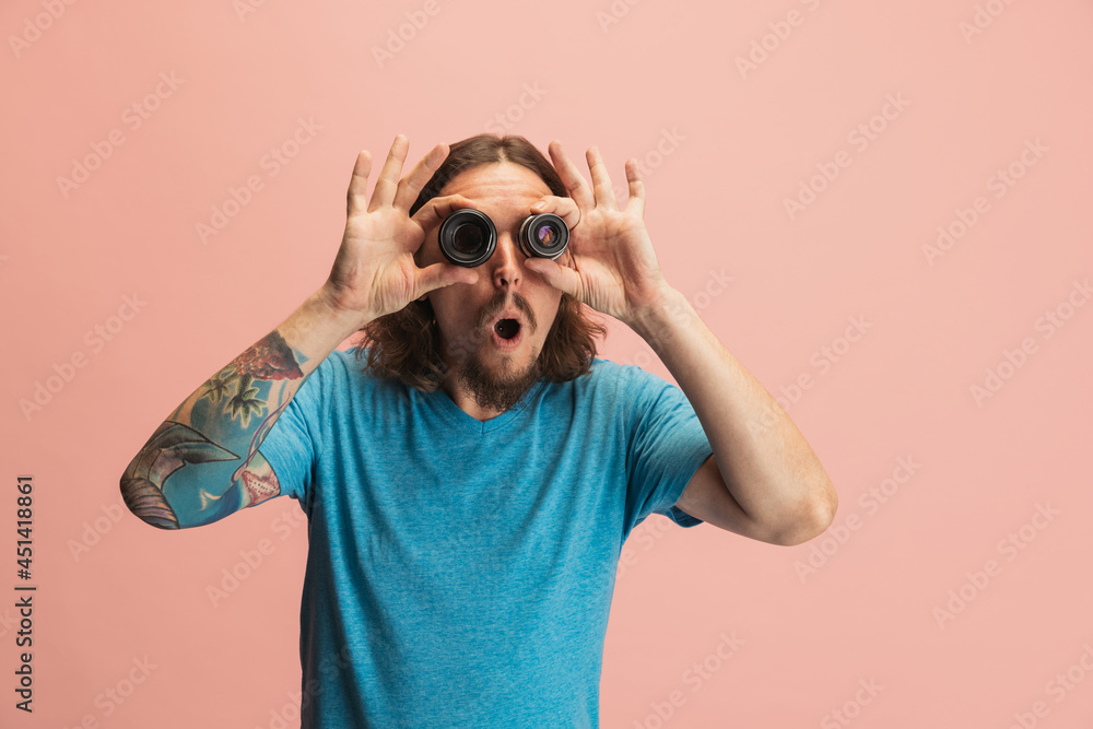 Portrait of young man, photographer, cameraman with camera lens having fun isolated on pink studio background. Concept of occupation, job, funny meme emotions