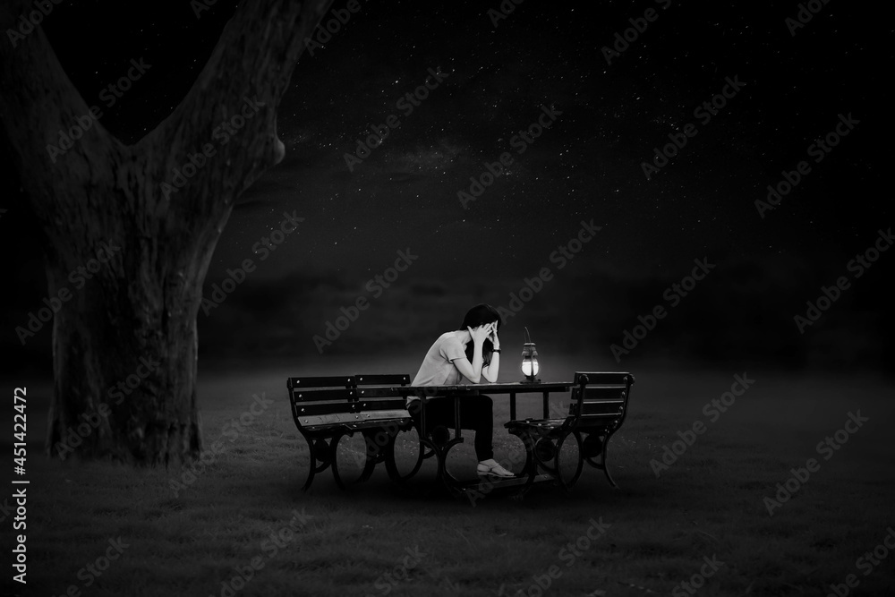 Fototapeta premium A black and white portrait of a young woman sitting on a chair lit by lanterns in the lonely night.