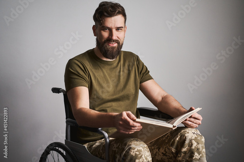 Happy military man sitting in a wheelchair and watching album photos